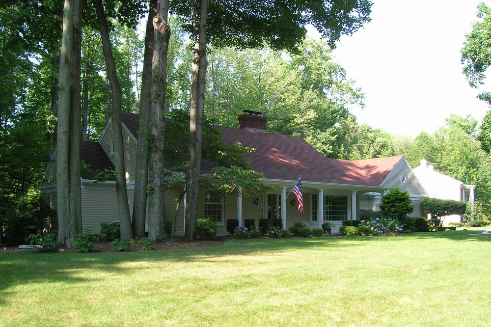 Sprawling tan ranch home with red roof refinished, set among trees in Erie County