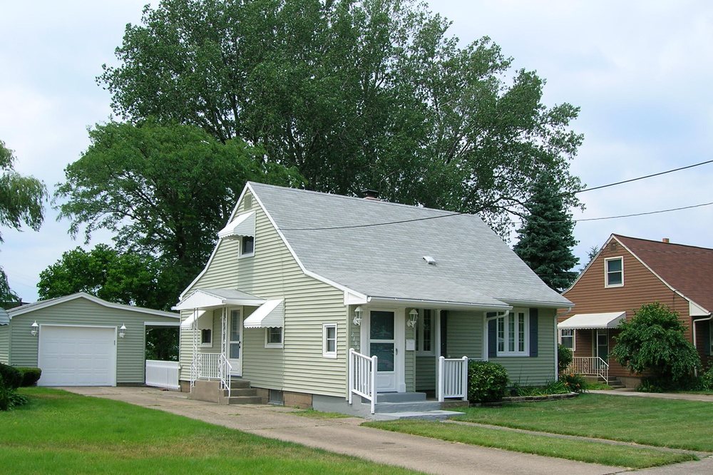 Sage-green Cape Cod home refinished with white trim and detached garage